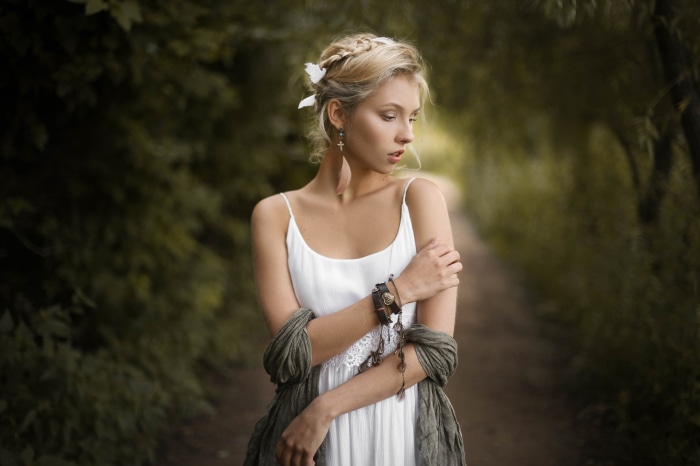 Woman with braided hair and white dress in a forest path