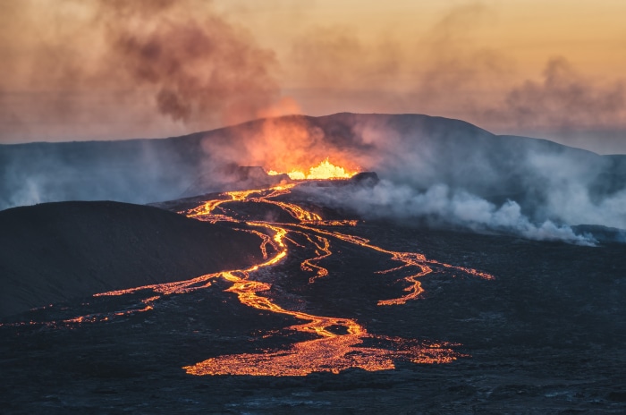 Volcano erupting with lava flow at sunset