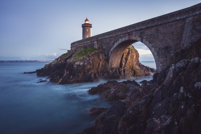 Lighthouse on a stone bridge over rocky coast