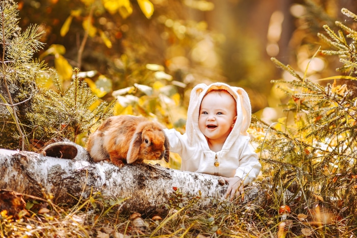 Baby in bunny costume with rabbit on log