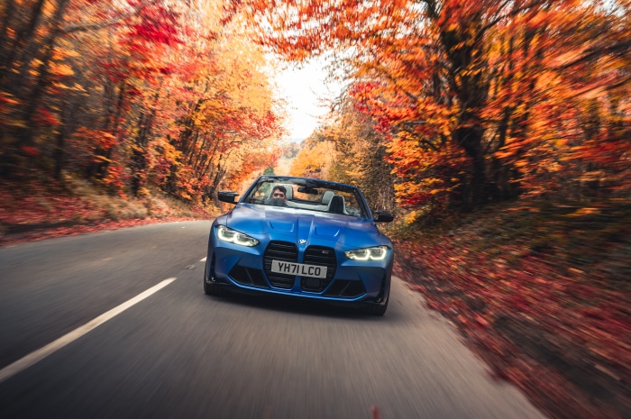 Blue BMW M4 Competition Convertible driving on autumn road