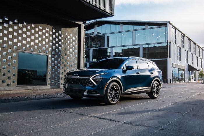 Blue Kia Sportage HEV SUV parked in front of modern buildings