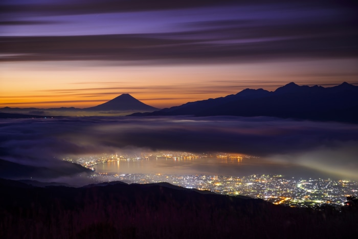 Mount Fuji and city lights at dawn over clouds