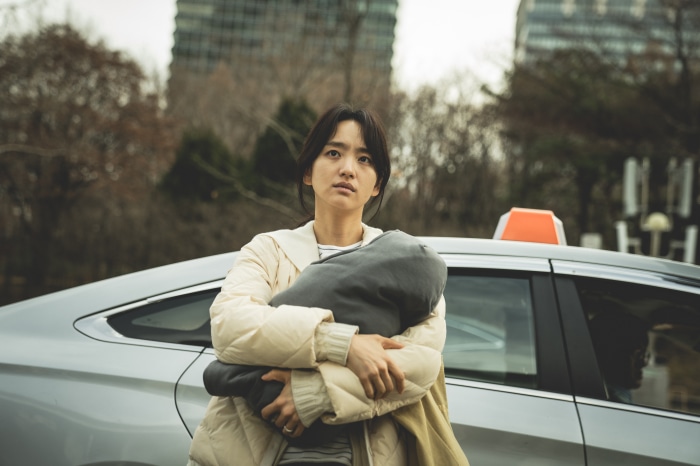 Woman holding a baby in front of a car in Hellbound 4K