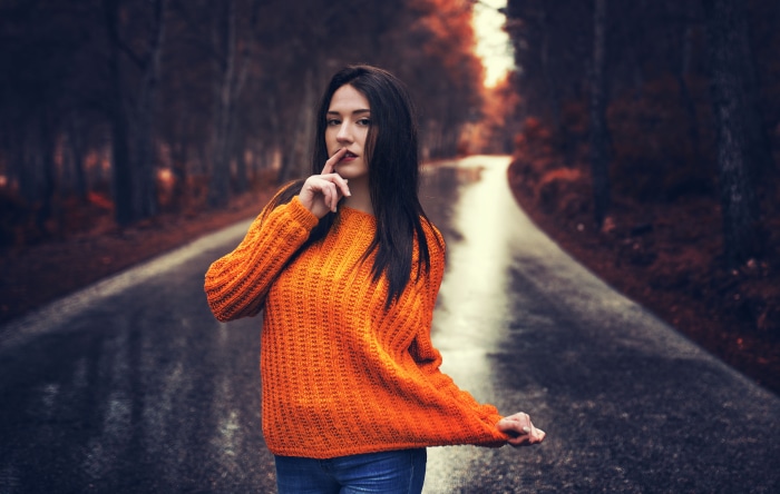Woman with black hair in orange sweater on road