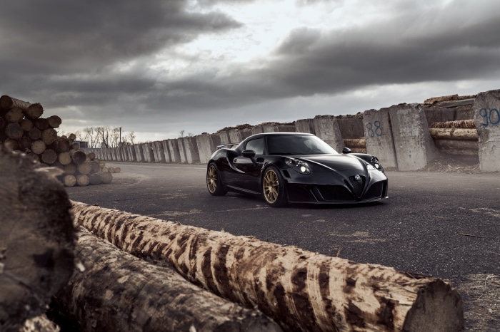 Black Alfa Romeo 4C on asphalt with logs and concrete barriers