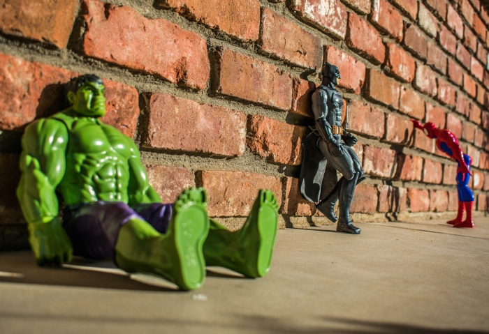 Hulk, Batman, and Spider-Man figures by a brick wall