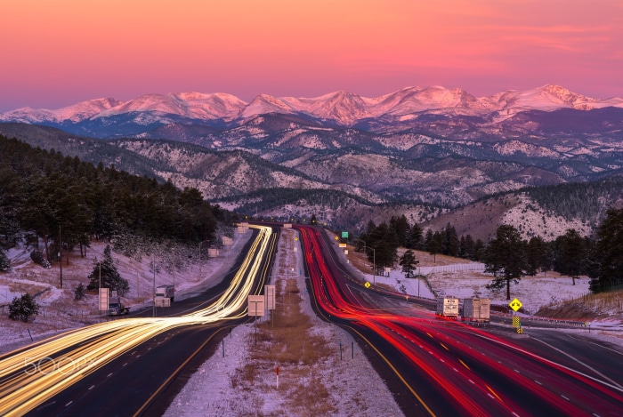 Time-lapse of highway traffic with snow-capped mountains at sunset
