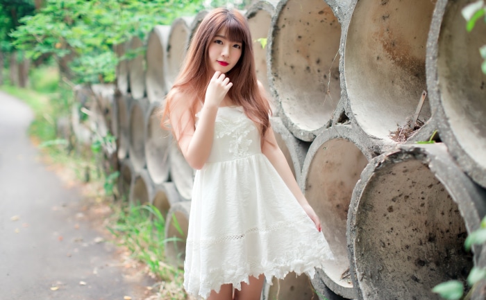 Asian woman in white dress near concrete pipes