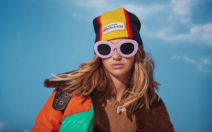 Model wearing sunglasses and beanie with Coach logo