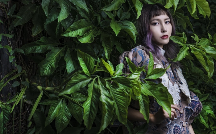 Asian woman in patterned dress among green leaves