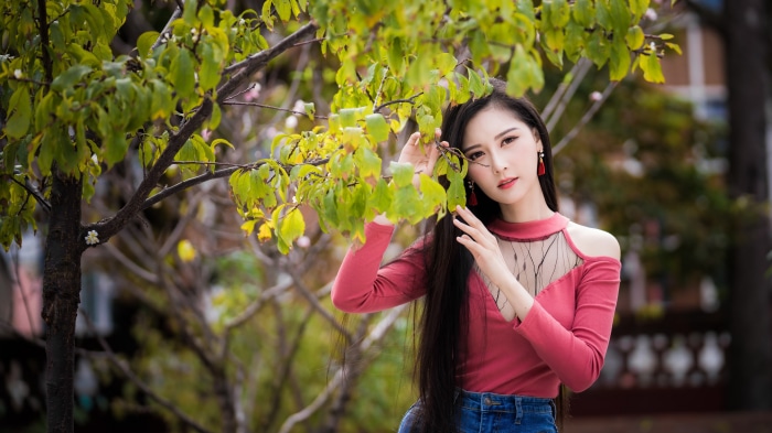Asian woman in pink shirt and jeans near tree