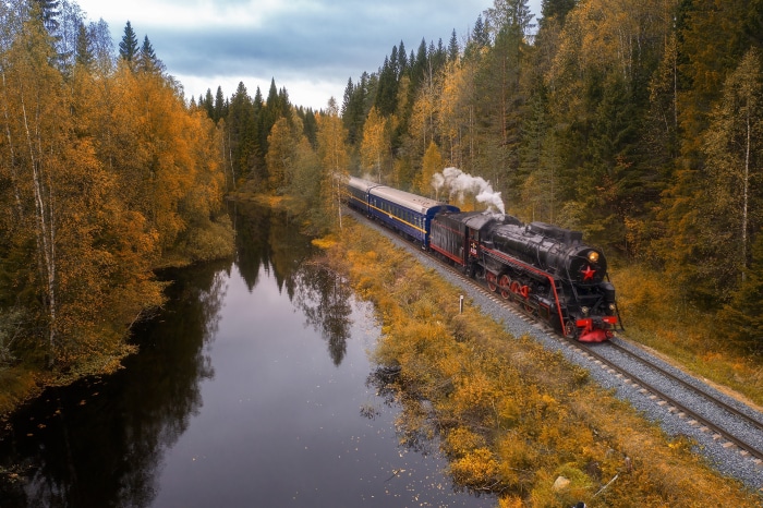 Steam train traveling through autumn forest by river