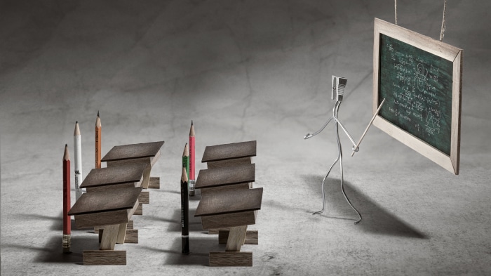 Pencils and desks in a classroom with a wire figure teacher