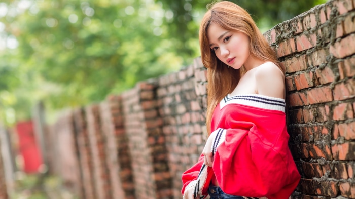 Asian woman in red top leaning against brick wall