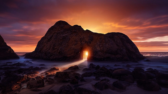 Sunset through a rock archway on a rocky beach