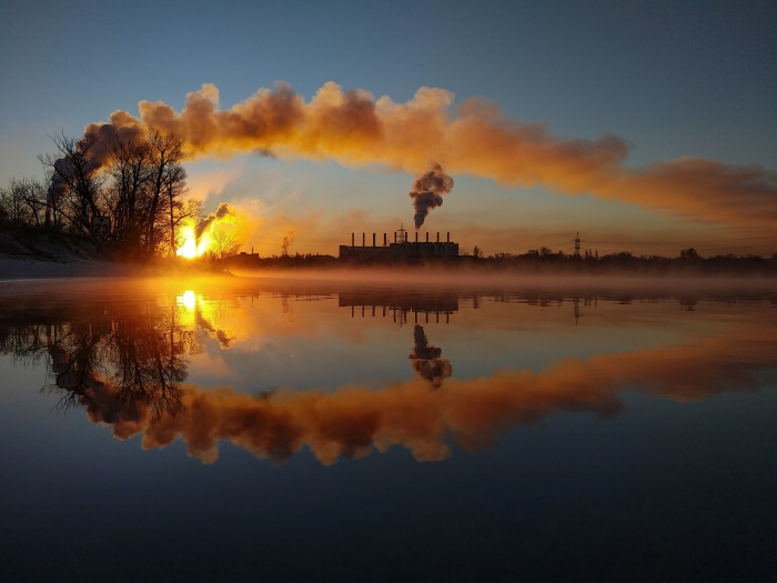 Industrial smoke stacks reflecting in water at sunrise