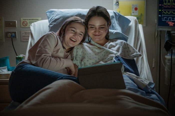 Two young women in a hospital room watching a tablet