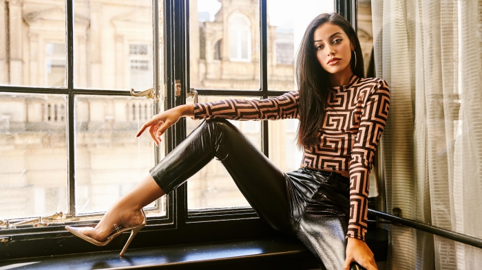 Woman with black hair wearing patterned top and leather pants