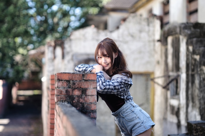 Asian girl with brunette hair leaning on a brick wall
