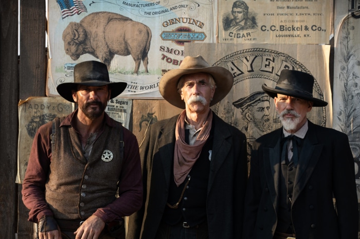 Three cowboys in front of vintage advertisements