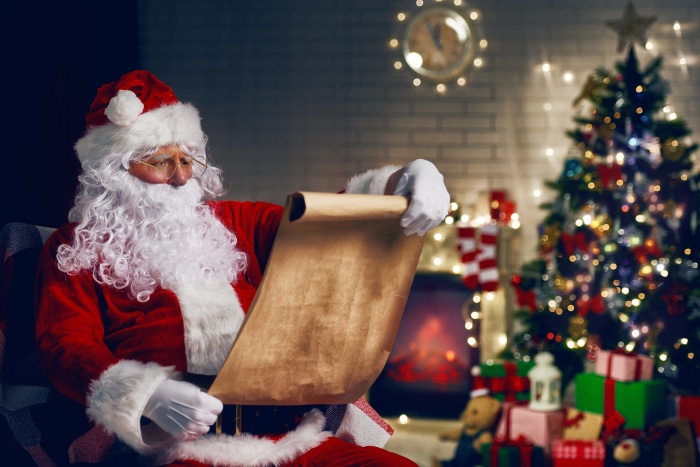 Santa Claus checking his list by a Christmas tree