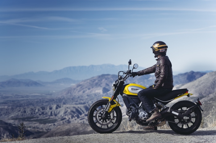 Man on yellow Ducati Scrambler motorcycle on mountain