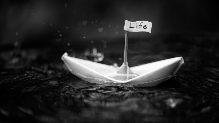 Origami paper boat with 'Life' flag in black and white