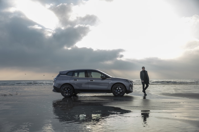 BMW iX M60 electric SUV on a beach with a man