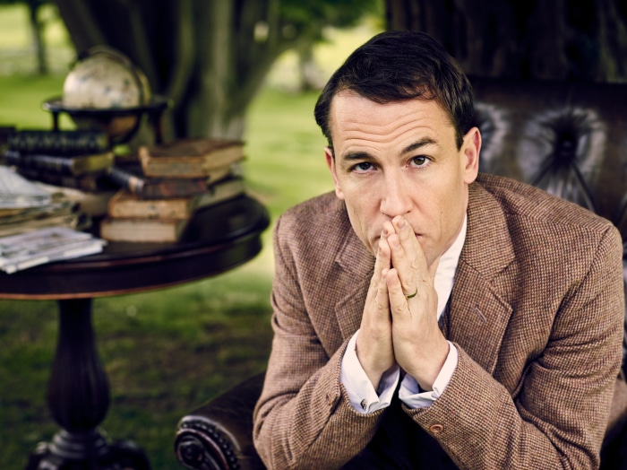 Man in a tweed jacket sitting in a chair