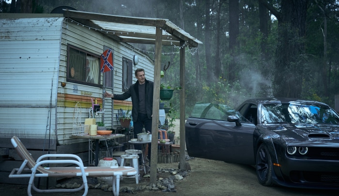 Liam Neeson in front of a trailer with a car