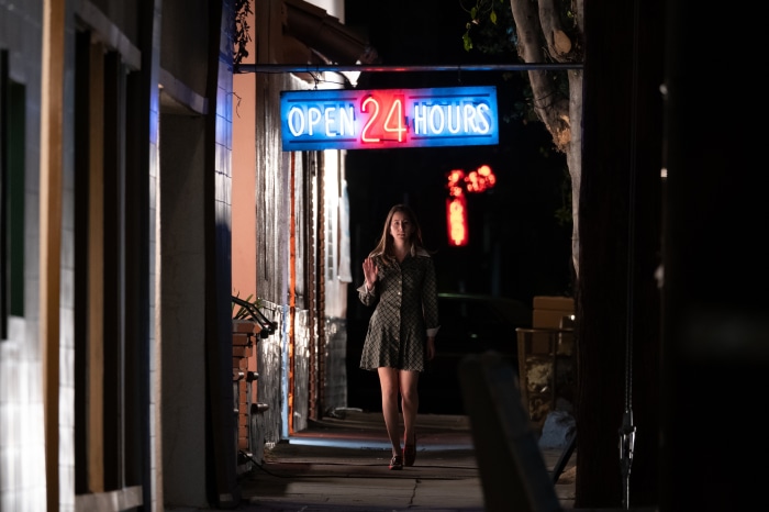 Alana Haim walking at night under an open 24 hours sign