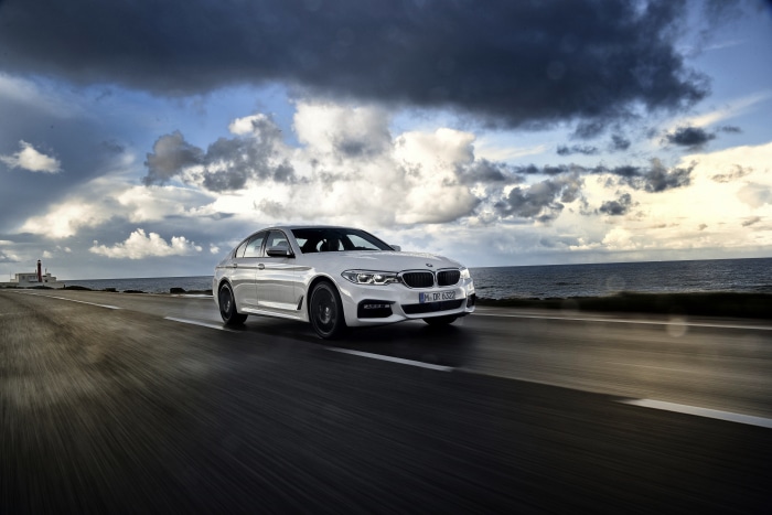 White BMW 5 Series driving on coastal road