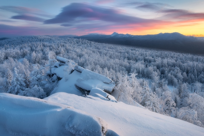 Winter forest landscape at sunrise with snow-covered trees and rocks