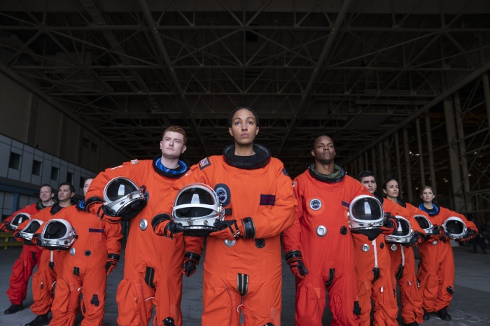 Astronauts in orange suits holding helmets