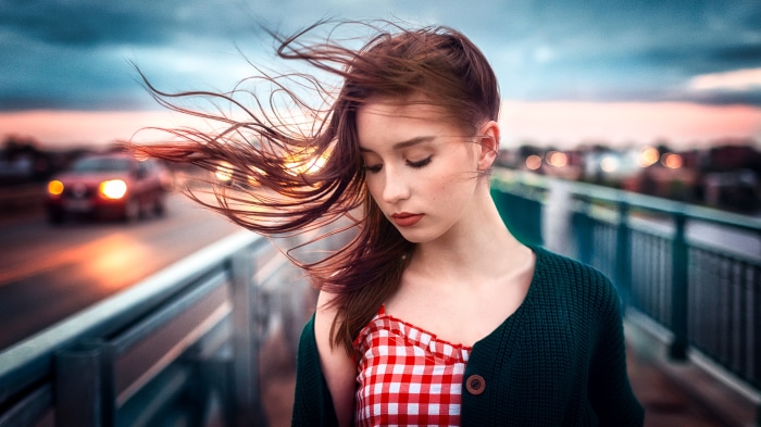 Young woman with windblown hair on a bridge at dusk