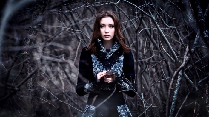Brunette woman holding a toad in a dark forest