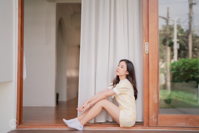 Asian woman in yellow dress sitting by window