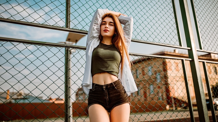 Woman in shorts and crop top leaning on fence