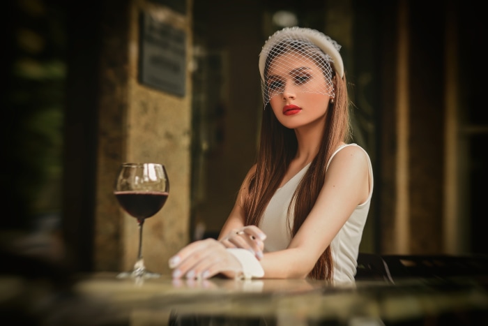 Woman with veil and red lipstick at a table with wine