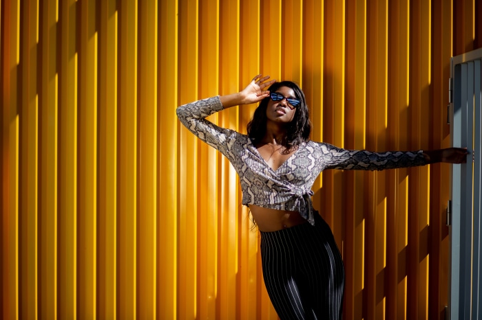Woman in snake print top and striped pants posing against yellow wall