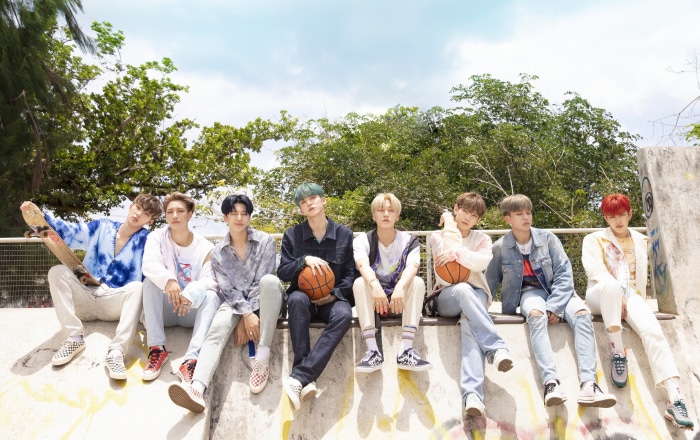 ATEEZ members sitting on a ledge outdoors