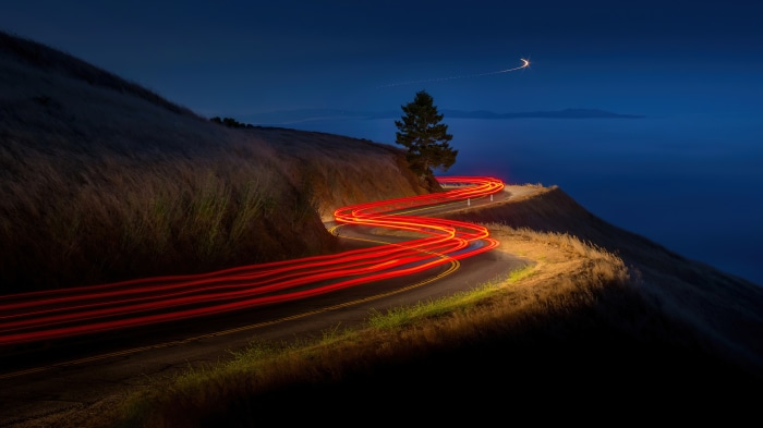 Night road with car light trails and ocean view