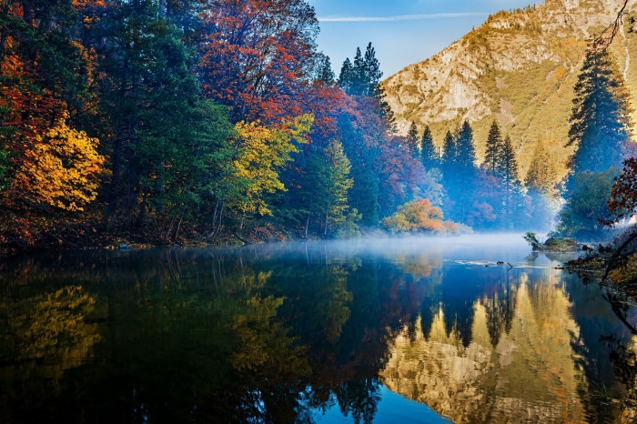 Autumn forest reflected in a misty lake with mountains