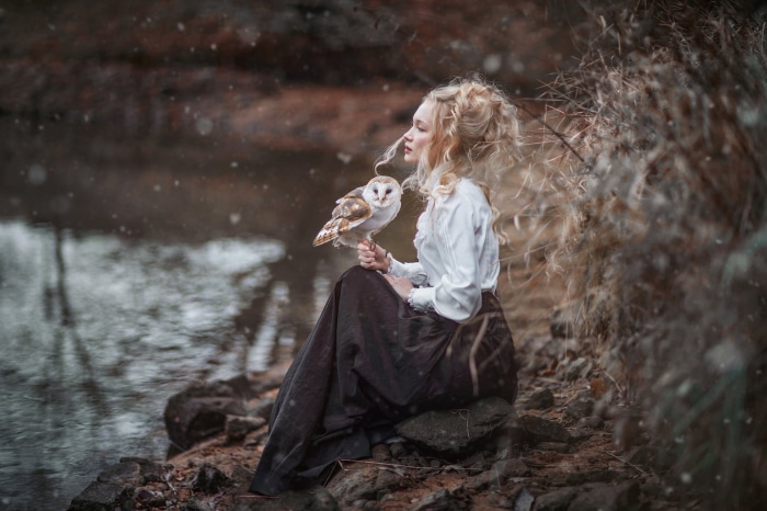 Woman holding an owl by a lake
