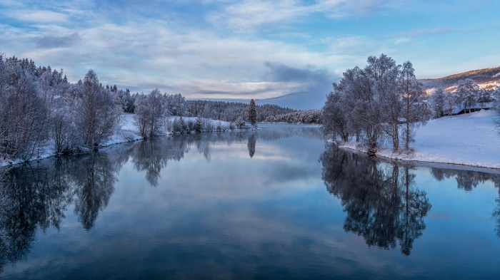 Winter river with snow-covered trees and reflections