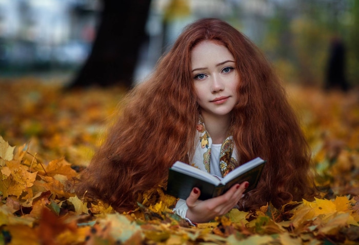 Redhead girl reading a book in autumn leaves