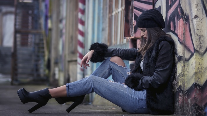 Woman in black beanie and ripped jeans sitting by graffiti wall