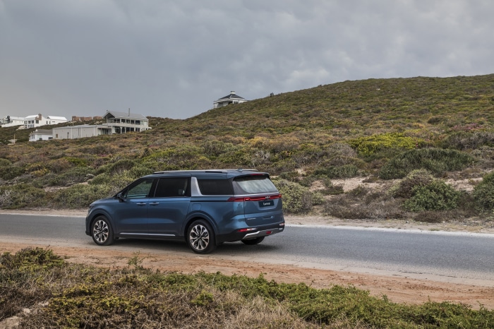 Blue Kia Carnival parked on a coastal road