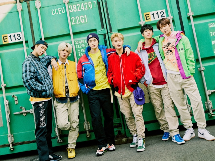 NCT members posing in front of a green shipping container